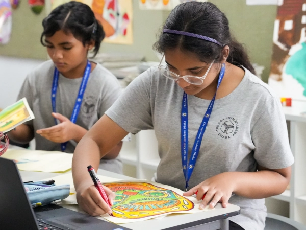 two students at AKA Dhaka focus on drawing and colouring during an art class.